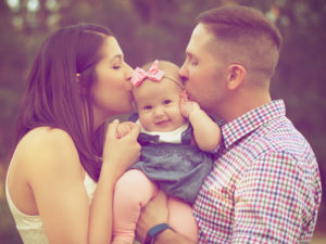Family portrait of parents kissing their smiling baby, emphasizing love and connection, relevant to the theme of individual impact on lives.